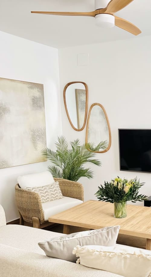 Moderna sala de estar en dúplex frente al mar en Málaga con silla de mimbre, espejo de madera, planta, TV y ventilador de techo