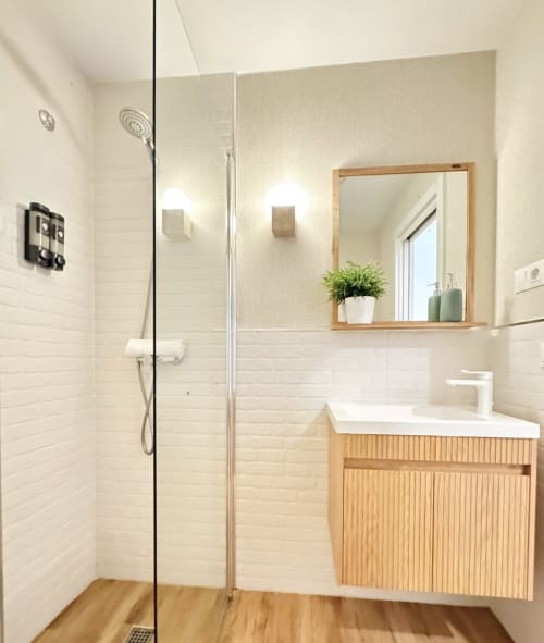 Baño moderno con azulejos blancos tipo metro, tocador de madera, espejo y ducha abierta en dúplex frente al mar de Málaga