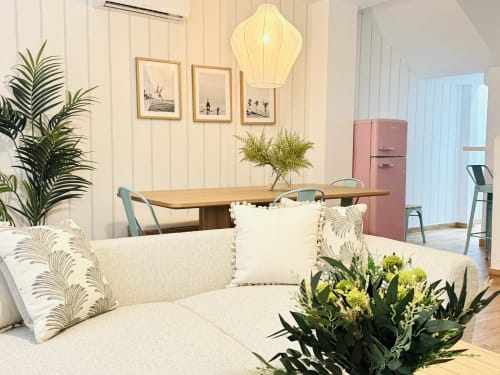 Luminoso salón diáfano con sofá crema, mesa de comedor de madera, nevera retro rosa y plantas en maceta en Málaga
