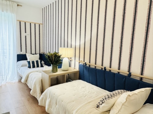 Moderno dormitorio en dúplex frente al mar en Málaga con cabeceros azules, papel tapiz rayado, mesita de madera y ropa de cama blanca