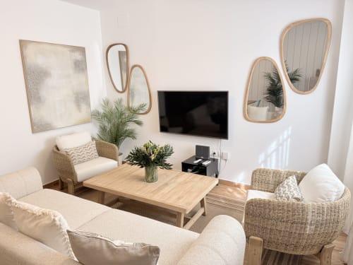 Salón moderno en dúplex frente al mar en Málaga con muebles de mimbre, mesa de madera, TV mural y espejos decorativos