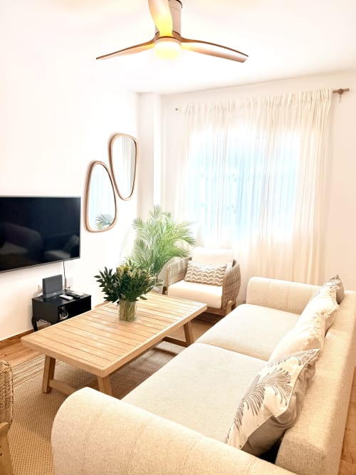Luminosa sala de estar frente al mar con asientos color crema, mesa de café de madera y vistas al mar en Sinese Design Homes, Málaga