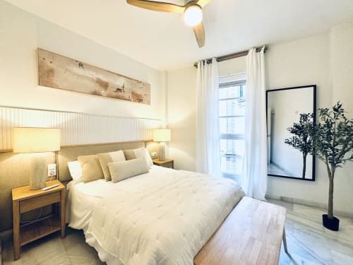 Dormitorio moderno y luminoso en apartamento lujo Catedral de Málaga con cama de matrimonio, mesitas de madera, ventilador de techo y balcón