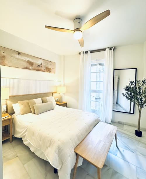Luminoso dormitorio en Málaga con ventilador de techo de madera, ropa de cama blanca y vistas a los monumentos por puertas francesas