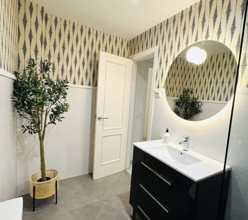 Baño moderno en apartamento Cathedral Deluxe, Málaga. Vanitory negro, espejo redondo, papel tapiz con patrón, azulejos blancos tipo metro.