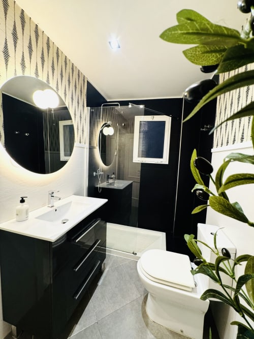 Baño moderno en blanco y negro con espejo redondo, lavamanos blanco, inodoro y ducha de lluvia en apartamento Cathedral Deluxe