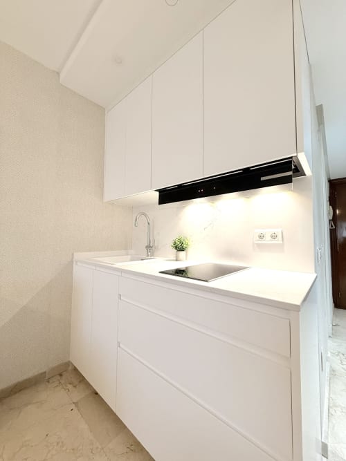 Cocina moderna blanca con fregadero de acero inoxidable y campana negra en apartamento de Torremolinos de Sinese Design Homes