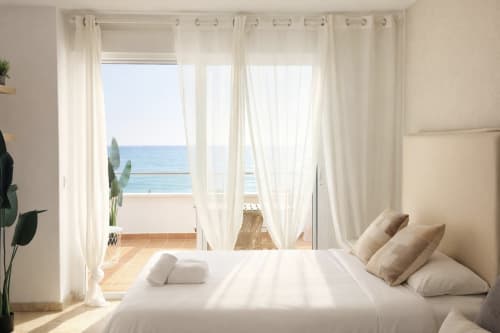 Luminoso dormitorio frente al mar con vistas al Mediterráneo, ropa de cama blanca, cortinas translúcidas y balcón en Torremolinos