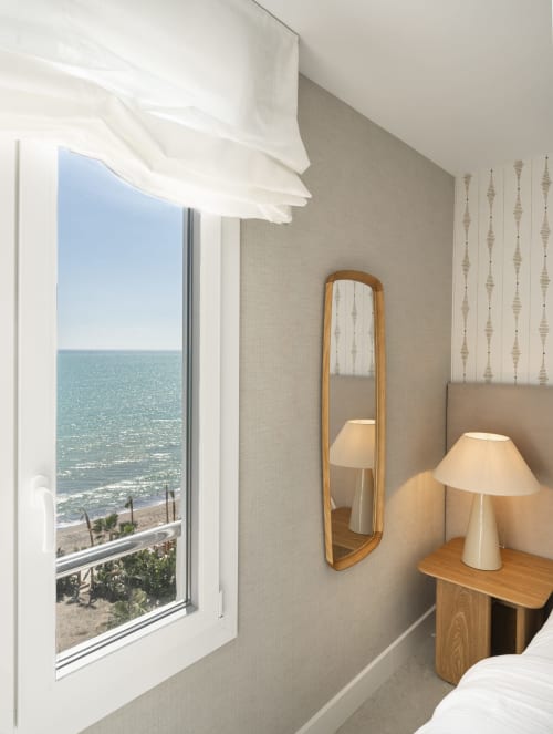 Luminoso dormitorio costero con vistas al mar, espejo de madera, lámpara de mesa y mobiliario moderno en Torremolinos
