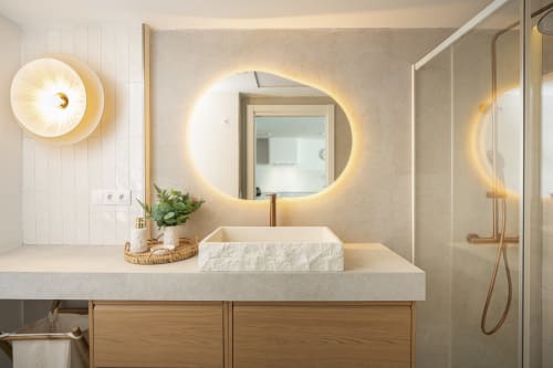 Lavabo moderno con espejo ovalado iluminado, lavamanos blanco tipo recipiente y muebles de madera en Sinese Design Homes, Torremolinos