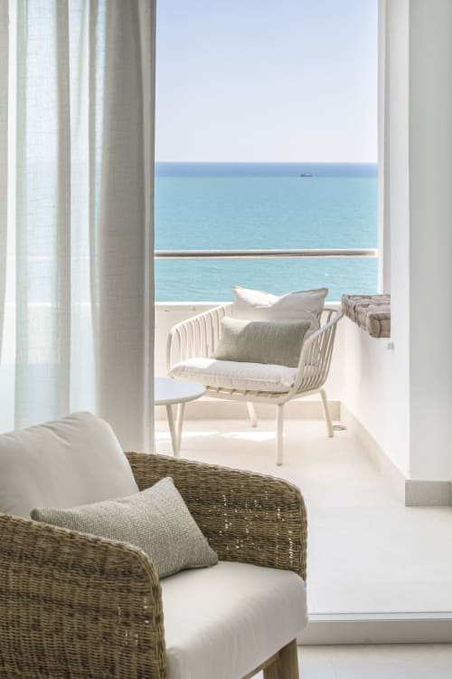 Terraza costera en ROCA Beach Torremolinos con sillas de mimbre, cortinas blancas y vistas al Mediterráneo