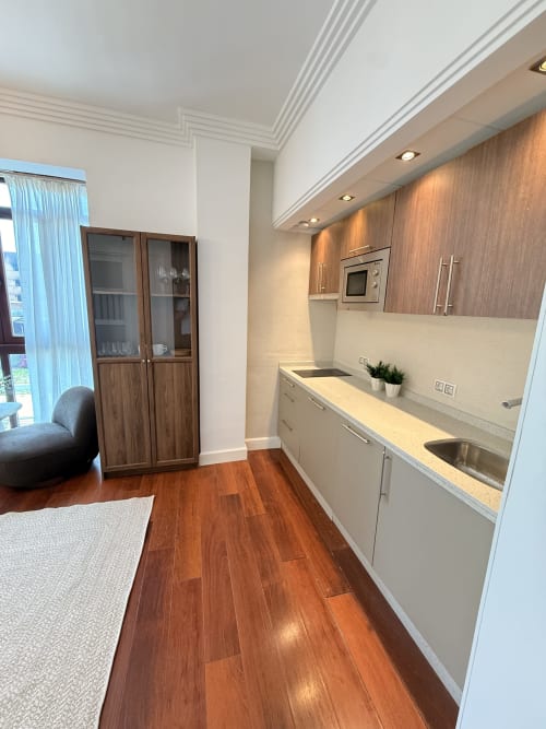 Cocina moderna en estudio de Málaga con muebles blancos, detalles en madera, electrodomésticos de acero inoxidable y pisos de madera