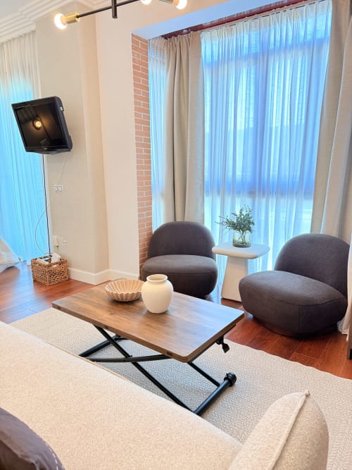 Sala de estar de apartamento moderno en Málaga con sillas grises redondas, mesa de café de madera y vistas a la ciudad