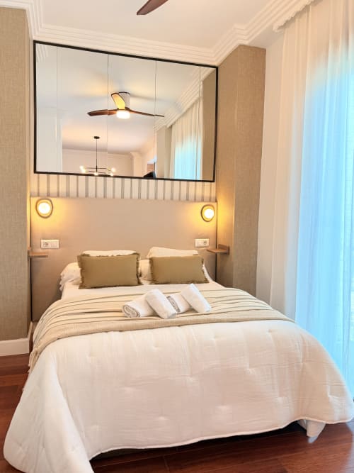Moderno dormitorio estudio en el centro de Málaga con cama queen, cabecero espejado, iluminación cálida y vistas a la ciudad