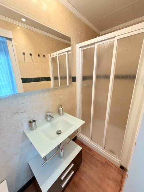 Moderno cuarto de baño en apartamento malagueño con lavabo blanco, espejo de gabinete y mampara de ducha con vidrio esmerilado