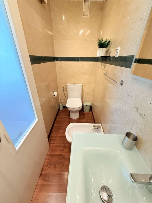 Baño moderno con azulejos de mármol beige, bañera blanca, inodoro y toallero calefactor en apartamento de Málaga