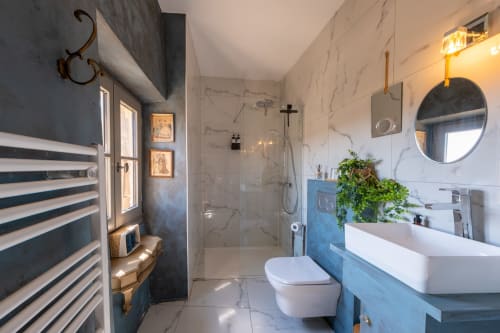Cuarto de baño moderno con azulejos de mármol, tocador azul, espejo redondo y ducha de lluvia en La vie de château B&B en Grignan