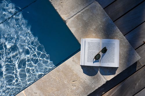 Open book and sunglasses by pool at La Maison & l'Orangerie B&B in Saint-Jean-des-Vignes