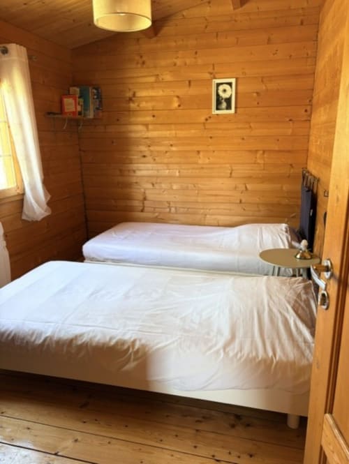 Chambre confortable du chalet en bois avec deux lits et draps blancs aux Chalets de Lozzi, Lozzi
