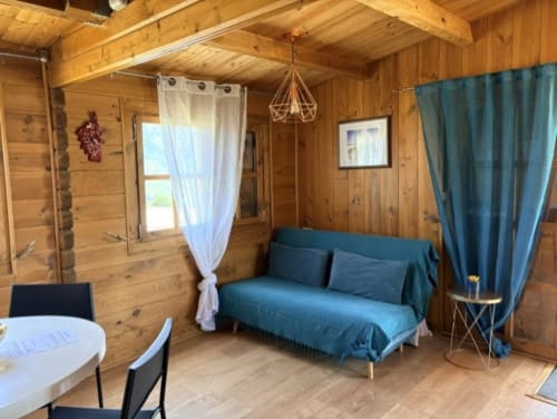 Intérieur chaleureux du chalet en bois avec canapé bleu, salle à manger et vue sur le jardin aux Chalets de Lozzi
