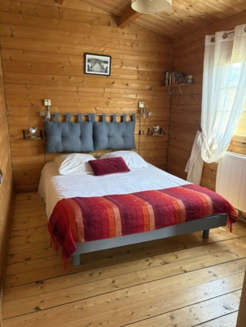Chambre cosy en bois au Chalet Golo des Chalets de Lozzi avec lit queen, tête de lit bleue, couverture rayée rouge et jardin