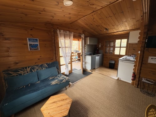 Intérieur douillet de chalet en bois avec canapé bleu, kitchenette et mobilier rustique aux Chalets de Lozzi, Corse