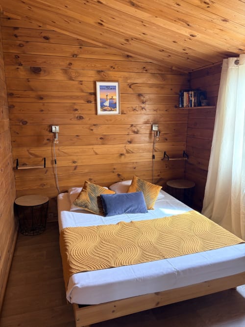Chambre douillette du chalet en bois avec lit queen-size, literie jaune à motifs et coussins décoratifs aux Chalets de Lozzi à Lozzi