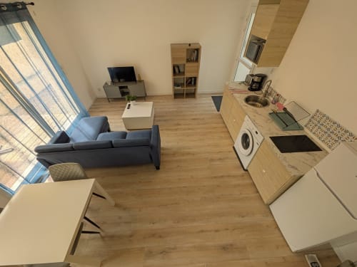 Studio ouvert à la Résidence des dunes avec cuisine, canapé bleu, TV et lumière naturelle par grande fenêtre