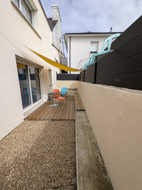 Petite cour avec terrasse en bois, chaises orange et bleu, voile jaune et murs crème au cottage Résidence des dunes