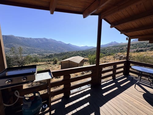 Terrasse en bois avec barbecue surplombant la vallée de Lozzi, les montagnes et le lac aux Chalets de Lozzi