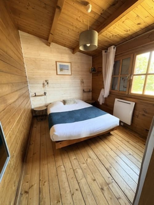 Chambre chaleureuse en bois du Chalet Niolu aux Chalets de Lozzi, avec lit queen-size, luminaire suspendu et vue sur les montagnes