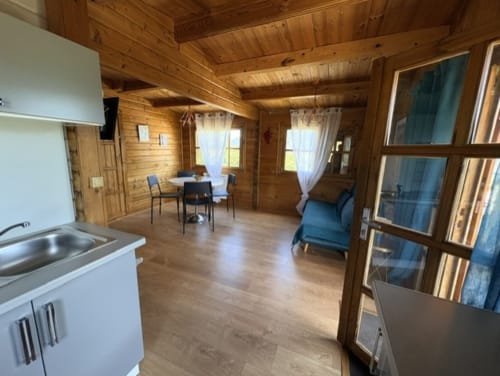 Intérieur spacieux du chalet en bois aux Chalets de Lozzi avec kitchenette, coin repas, fauteuil bleu et grandes fenêtres