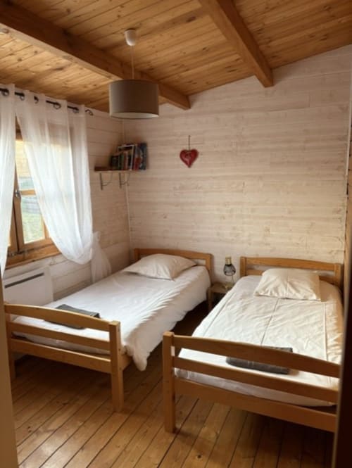Chambre chaleureuse du chalet en bois avec deux lits simples, plafond aux poutres apparentes et vue sur le lac aux Chalets de Lozzi, Corse