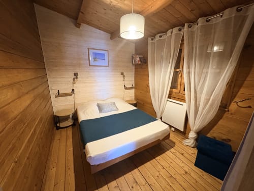 Chambre chaleureuse en bois aux Chalets de Lozzi avec lit queen, voilages et luminaires suspendus à Lozzi, France