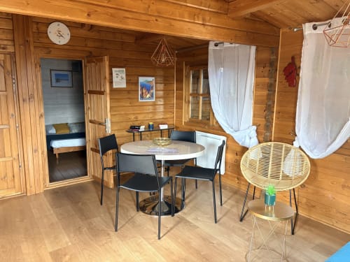 Intérieur du chalet en bois aux Chalets de Lozzi avec table à manger, chaises et entrée de chambre à Lozzi, France