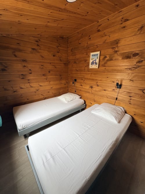 Chambre chaleureuse du chalet en bois avec deux lits et linge blanc aux Chalets de Lozzi, Corse