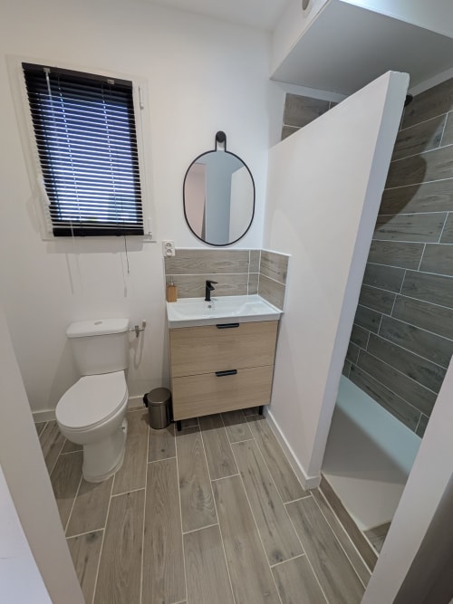 Salle de bain moderne à la Résidence des dunes avec lavabo, toilettes, carrelage imitation bois et douche à l'italienne