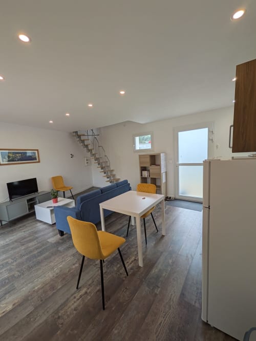 Séjour contemporain avec salle à manger, canapé bleu, chaises jaunes, cuisine et escalier à la Résidence des dunes