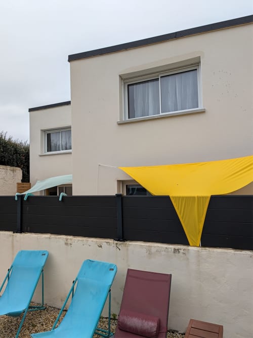 Cottage moderne à la Résidence des dunes à Landéda avec transats bleus, clôture noire et voile solaire jaune
