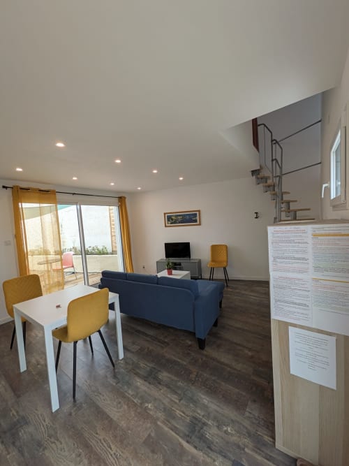 Salon moderne de la Résidence des dunes avec canapé bleu, table à manger, téléviseur et portes vitrées ouvrant sur la terrasse