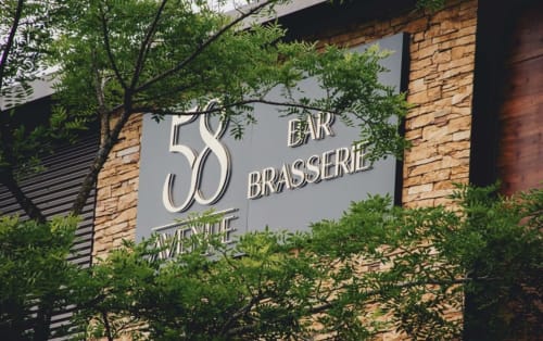 Enseigne du Bar Brasserie 58 à l'hôtel Les séjours Ardennais à Renwez, France avec mur de brique et verdure