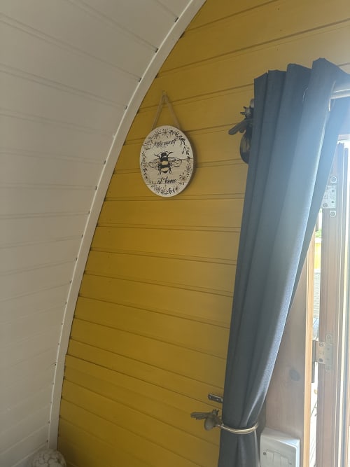 Yellow wooden wall in Bumblebee Pod at Acorns Luxury Glamping with bee-themed oval sign and blue curtains