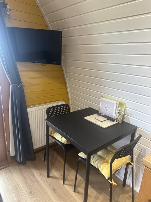 Bumblebee Pod dining area at Acorns Luxury Glamping with black table, chairs, wall-mounted TV, and yellow accents