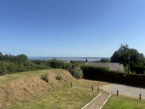 Acorns Luxury Glamping sea view showing manicured grounds, deck, and distant coastline under clear sky