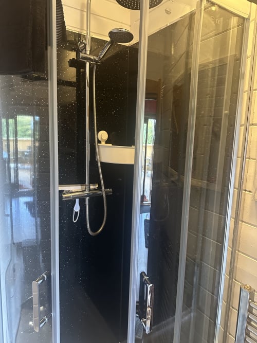 Modern shower enclosure with black speckled walls and chrome fixtures in Bumblebee Pod at Acorns Luxury Glamping, Holywell
