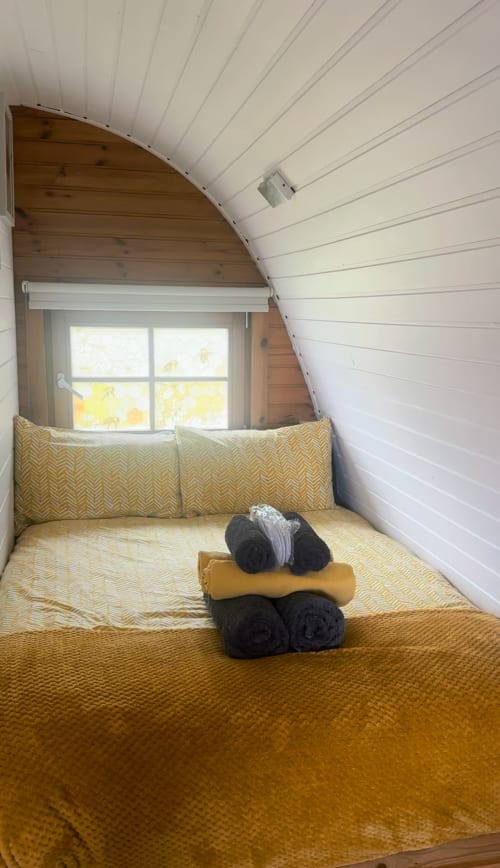 Cozy bedroom nook in Bumblebee Pod at Acorns Luxury Glamping, Holywell, with mustard yellow bedding and window view