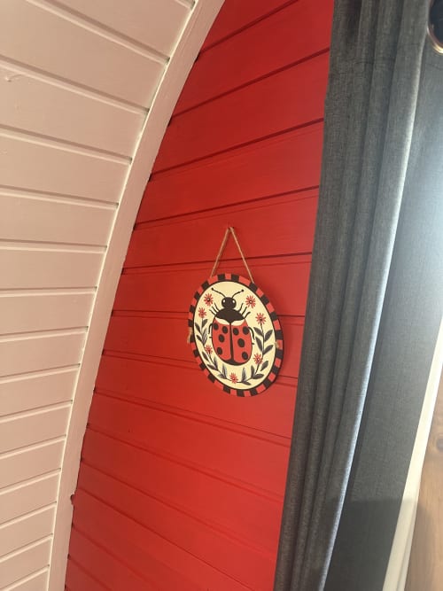 Red door of Ladybird Pod at Acorns Luxury Glamping with decorative ladybug wall hanging in Holywell