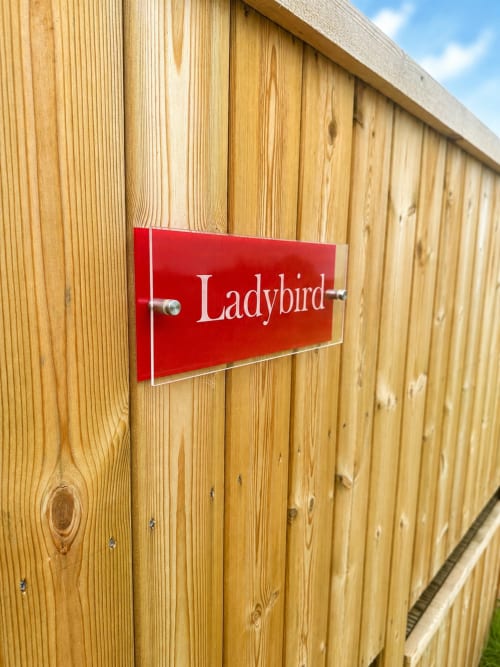 Red 'Ladybird' nameplate on wooden door at Acorns Luxury Glamping pod in Holywell, GB