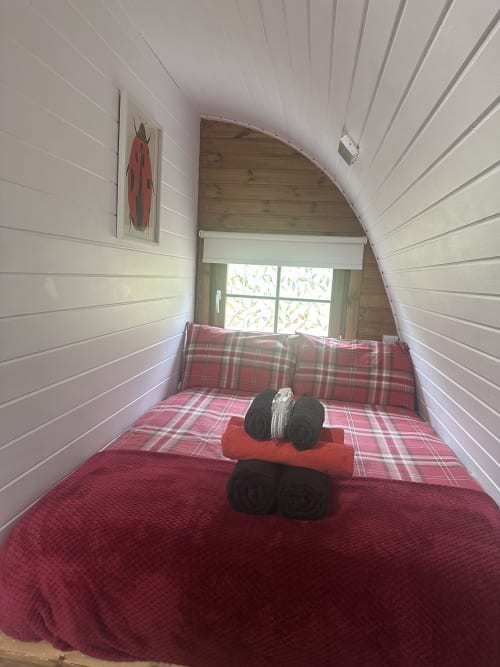 Cozy Ladybird Pod bedroom at Acorns Luxury Glamping with red tartan bedding, white wooden walls, and arched window