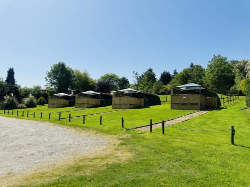 Acorns Luxury Glamping pods in Holywell garden with green lawns and trees under clear blue sky